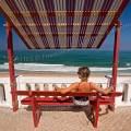001282 Jeune femme assise sur un banc et sous un auvent, de dos, face  l'ocan Atlantique (Lisboa e Vale do Tejo, Portugal). 