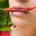 001591 Jeune femme tenant un petit piment rouge (Capsicum annuum) dans sa bouche.