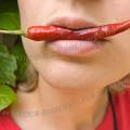 001592 Jeune femme tenant un petit piment rouge (Capsicum annuum) dans sa bouche.