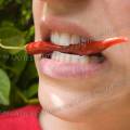 001593 Jeune femme tenant serr entre ses dents un petit piment rouge (Capsicum annuum) dans sa bouche.