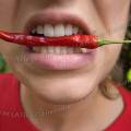 001595 Jeune femme tenant serr entre ses dents un petit piment rouge (Capsicum annuum) dans sa bouche.