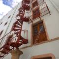 001714 Escalier de secours en colimaon, de couleur rouge, se dployant sur une faade blanche. La base de l'escalier est soutenue par une colonne en pierre, ancienne. Des portes en bois, identiques, se superposent de bas en haut du btiment (Guanajuato, Mexique).